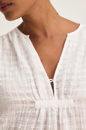 A close-up of someone wearing the KORA TEXTURED COTTON GAUZE TOP by Velvet by Graham & Spencer, highlighting its lightweight fabric and small V-neckline secured with a clasp.