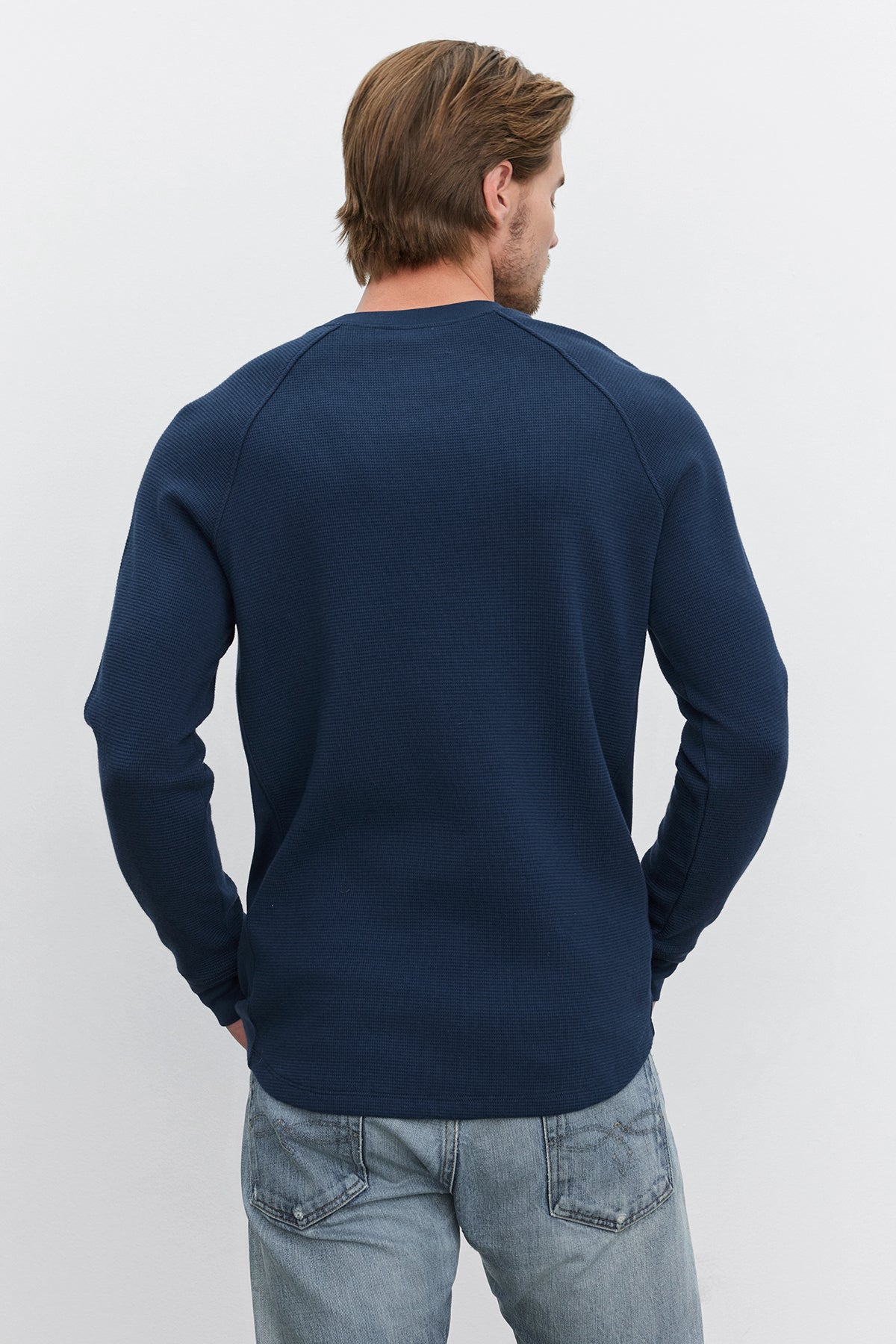   A person with light brown hair is standing with their back to the camera, wearing a Velvet by Graham & Spencer GLEN THERMAL CREW in dark blue and light blue jeans. 