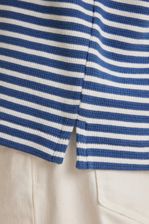 Close-up of the HARLAN THERMAL STRIPED CREW by Velvet by Graham & Spencer, featuring blue and white stripes with a small side split, paired with white pants.