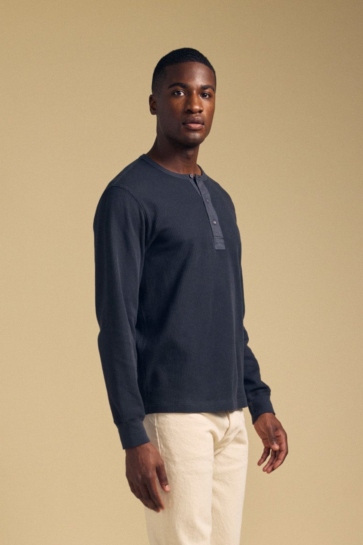 Front view of a man wearing the graphite CHANCE THERMAL HENLEY showcasing its button placket and long sleeves with a beige background