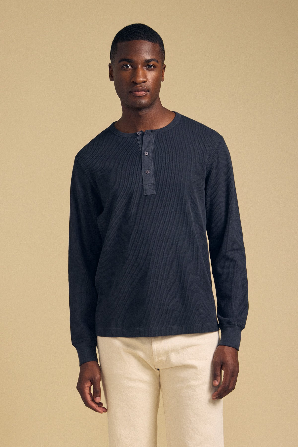 A man wearing a dark blue CHANCE THERMAL HENLEY by Velvet by Graham & Spencer, featuring a button placket, paired with light-colored pants.-46288227336385