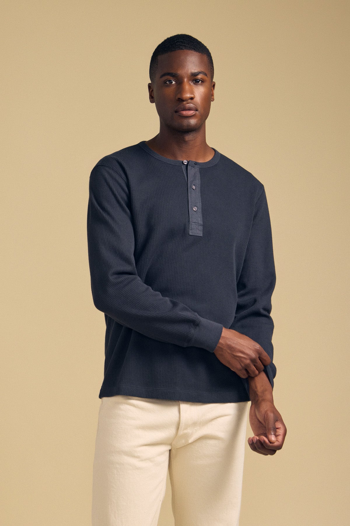 A man wearing a dark-colored, long-sleeved CHANCE THERMAL HENLEY by Velvet by Graham & Spencer with a button placket and light-colored pants, perfect for cold-weather wear.