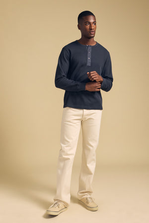 A man wearing a dark blue 100% cotton CHANCE THERMAL HENLEY by Velvet by Graham & Spencer, light-colored pants, and sneakers.