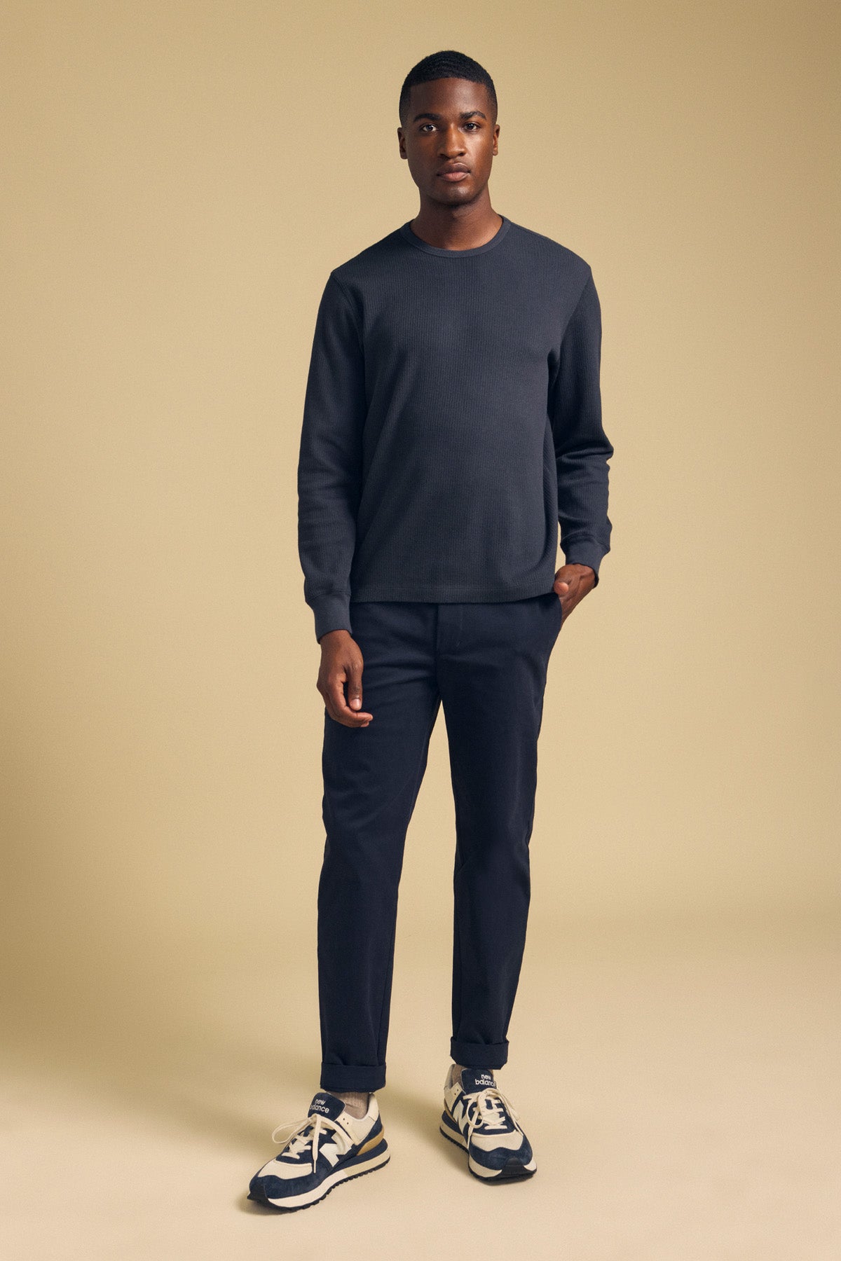 A man wearing a dark blue long-sleeved DARIEL THERMAL PULLOVER, dark trousers, and athletic sneakers, styled as a cold-weather essential.