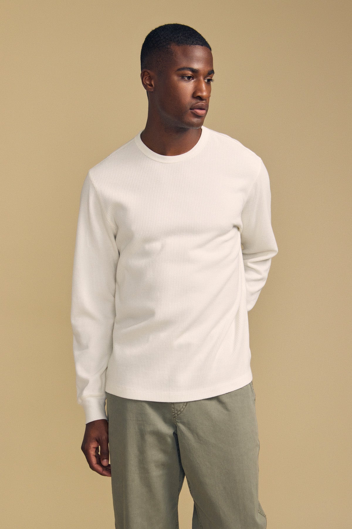A man wearing the DARIEL THERMAL PULLOVER by Velvet by Graham & Spencer and olive pants stands against a beige background, looking slightly to the side.-41859630825665