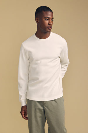 A man wearing the DARIEL THERMAL PULLOVER by Velvet by Graham & Spencer and olive pants stands against a beige background, looking slightly to the side.