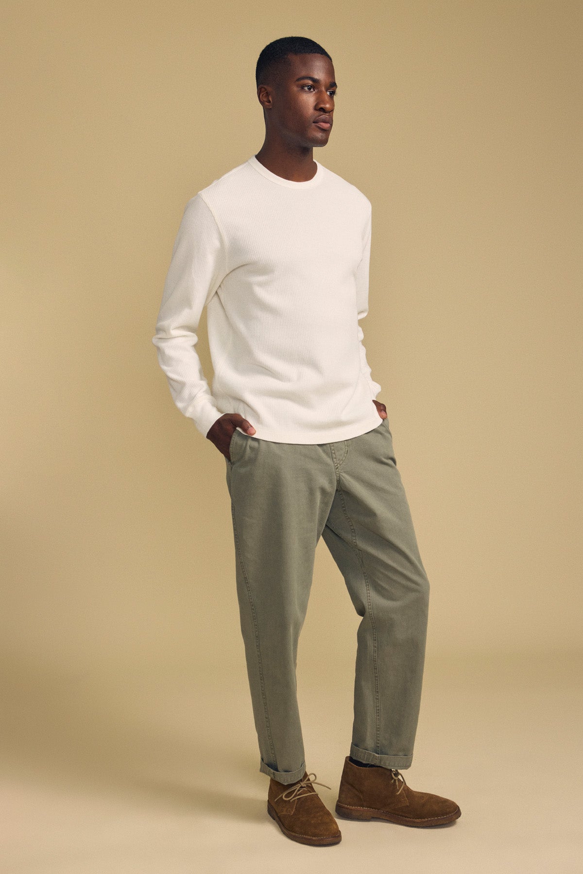 A person stands against a beige background wearing the Velvet by Graham & Spencer DARIEL THERMAL PULLOVER, paired with olive green pants and brown suede shoes, with hands in pockets.