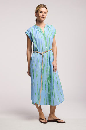 Model wears the JADA DRESS by Velvet by Graham & Spencer: a light blue, short-sleeved, knee-length midi with green vertical stripes and a thin belt, styled with brown sandals for effortless California flair against a plain backdrop.