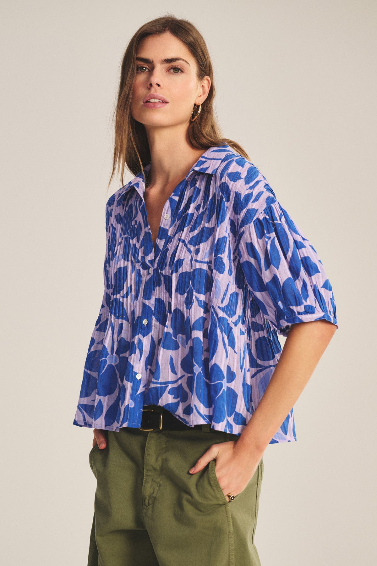 A woman wears the TILDA TOP by Velvet by Graham & Spencer, a loose blue and lavender floral cotton blouse with pleats and three-quarter sleeves, paired with olive green pants against a neutral background.-40808748974273