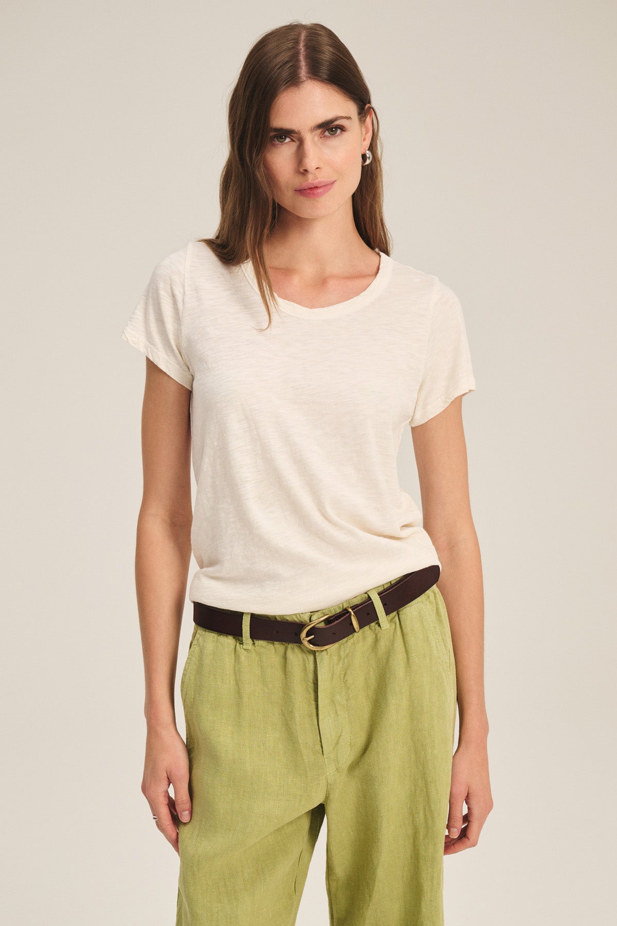 A woman faces forward wearing the TILLY TEE by Velvet by Graham & Spencer, a cream cotton slub crewneck top, tucked into light green pants with a dark belt, set against a plain background.