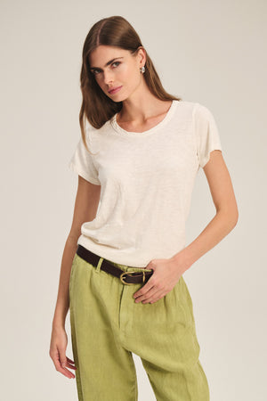 A woman wears the TILLY TEE by Velvet by Graham & Spencer—a relaxed fit, cotton slub crewneck—tucked into light green pants with a black belt, standing against a neutral background.