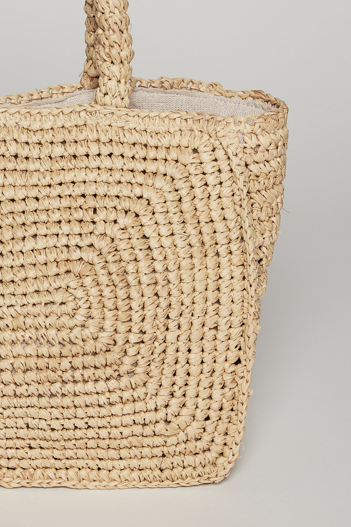   Close-up of a durable TINA STRAW TOTE BAG with sturdy twisted handles, featuring a detailed spiral pattern and texture by Velvet by Graham & Spencer. 
