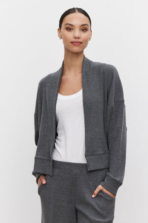 A person wearing an ultra-soft and cozy Velvet by Graham & Spencer LYNNETTE RIBBED CARDIGAN in grey over a white top with matching grey ribbed pants, standing against a plain light background.