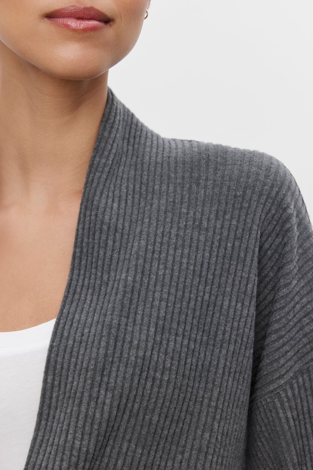   Close-up of a person wearing the ultra-soft and cozy LYNNETTE RIBBED CARDIGAN by Velvet by Graham & Spencer in gray, layered over a white shirt. The image focuses on the lower face and upper torso. 