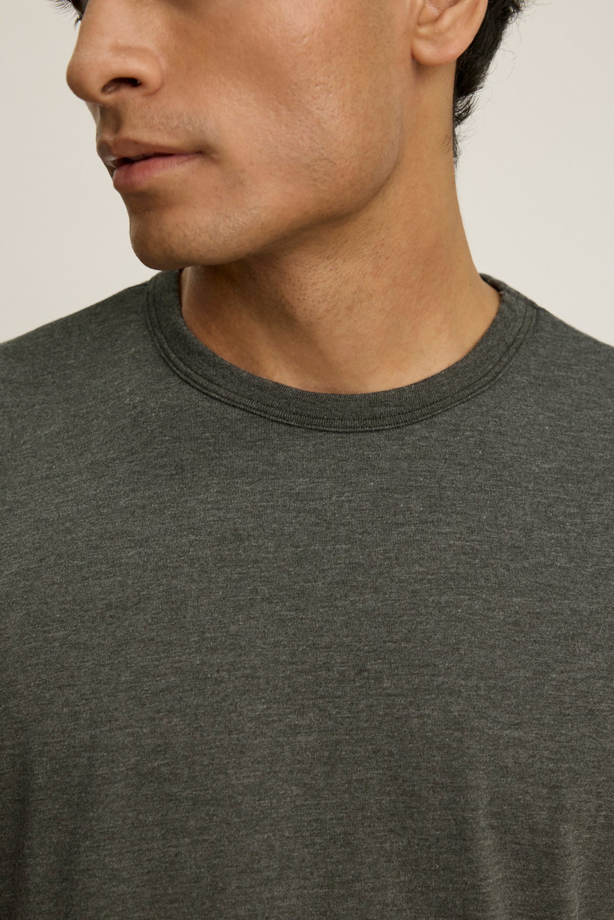 A close-up of a person wearing the ZANDER TEE by Velvet by Graham & Spencer—a plain dark gray, relaxed-fit t-shirt with a ribbed crew neckline—showing the lower half of their face and upper torso.-39446055059649