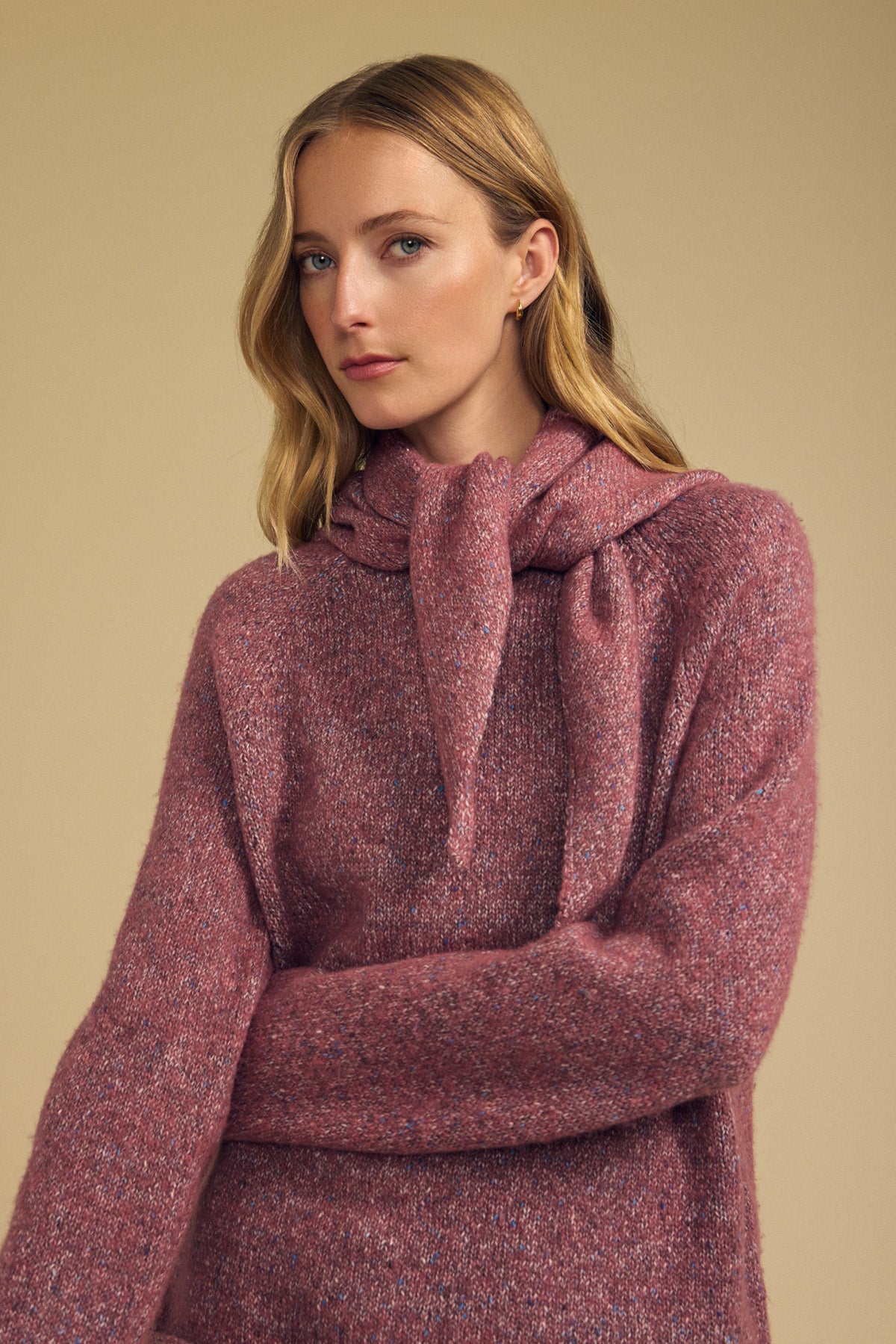 Woman with long blonde hair wearing the KARLA SCARF from Velvet by Graham & Spencer, its textured mauve wool blend draped loosely over her shoulders, standing against a beige background.-42063771009217