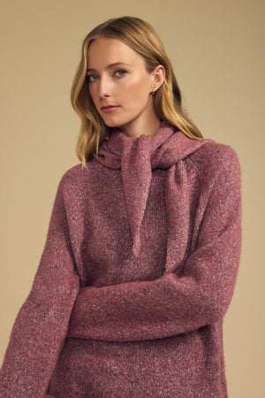 Woman with long blonde hair wearing the KARLA SCARF from Velvet by Graham & Spencer, its textured mauve wool blend draped loosely over her shoulders, standing against a beige background.