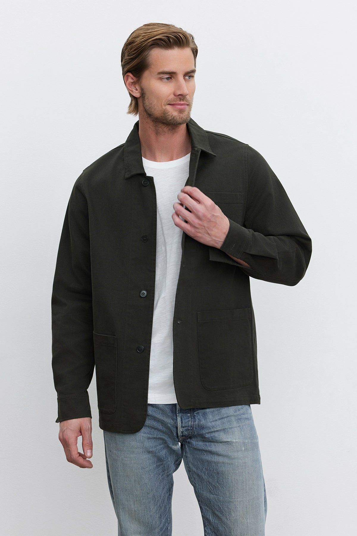   A person with brown hair wears a dark green BARCLAY CHORE JACKET by Velvet by Graham & Spencer, made of mid-weight cotton lyocell twill, over a white shirt and blue jeans. They stand against a plain white background, facing slightly to the left. 