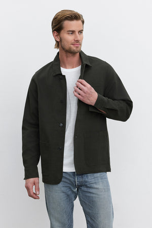 A person with brown hair wears a dark green BARCLAY CHORE JACKET by Velvet by Graham & Spencer, made of mid-weight cotton lyocell twill, over a white shirt and blue jeans. They stand against a plain white background, facing slightly to the left.