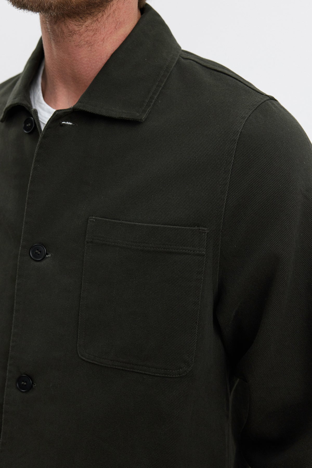   A person wearing the BARCLAY CHORE JACKET from Velvet by Graham & Spencer, made from mid-weight dark green cotton lyocell twill with a front chest pocket, and a white shirt underneath. 