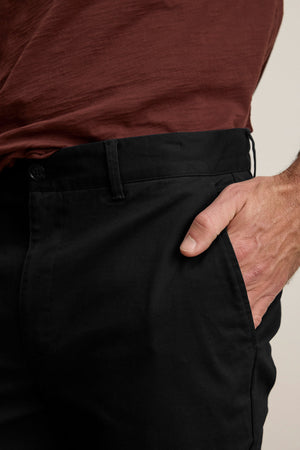 A person showcases a polished look, wearing the MADDOX PANT by Velvet by Graham & Spencer with their right hand in their pocket and paired with a maroon shirt.