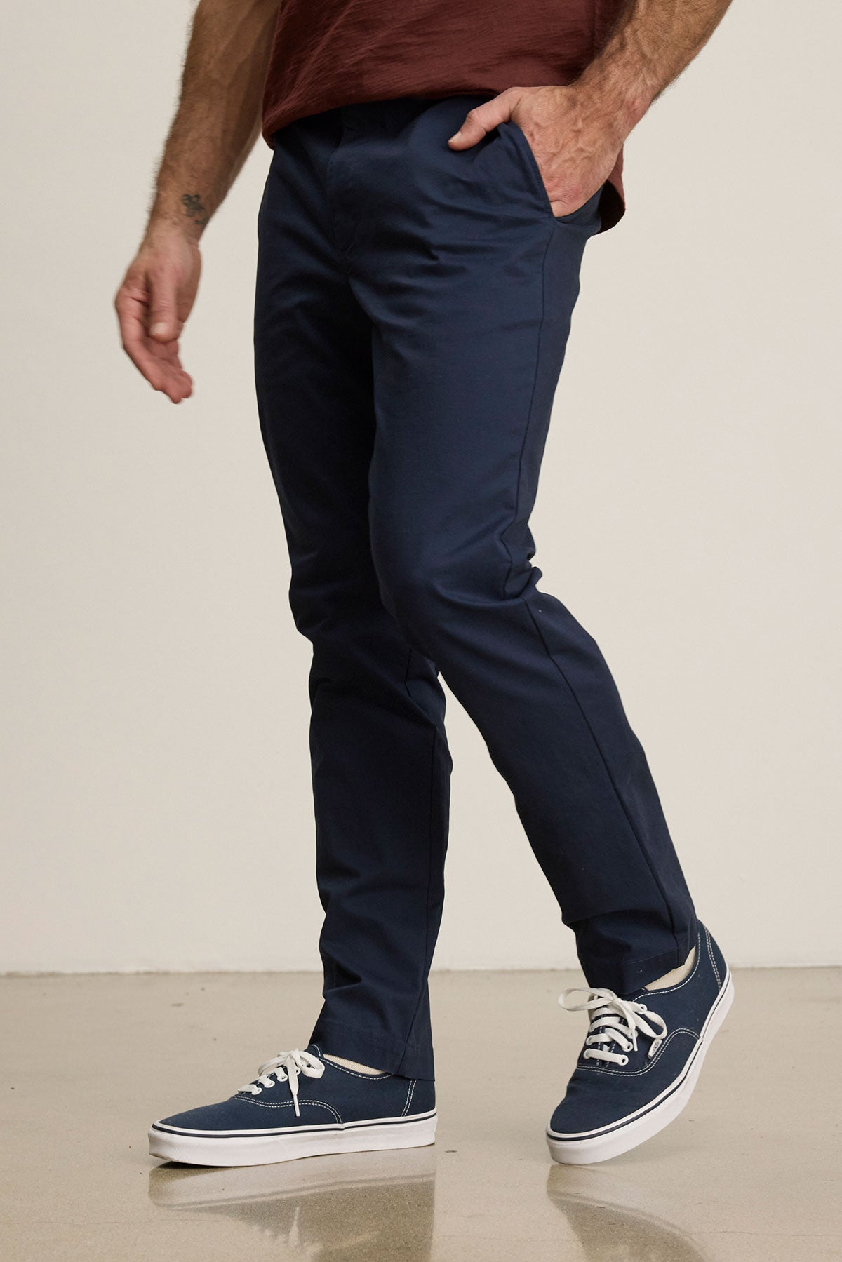 Someone stands on a light floor against a plain background wearing Velvet by Graham & Spencer's MADDOX PANT in tailored navy stretch cotton twill and navy sneakers with white laces, creating a polished look.