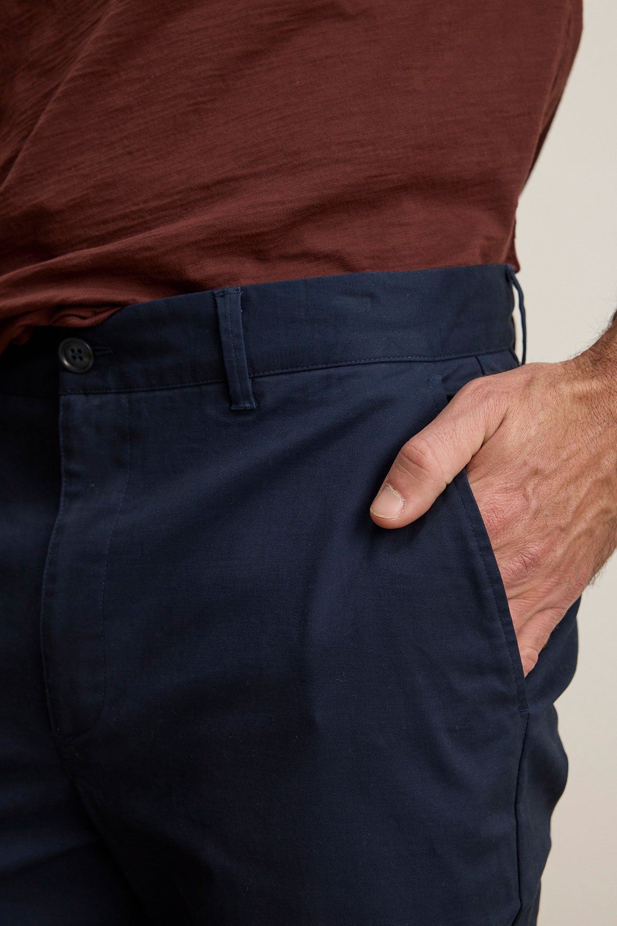 A person wears Velvet by Graham & Spencer's MADDOX PANT in navy blue stretch cotton twill and a brown shirt, with their right hand in the pocket for a polished look.