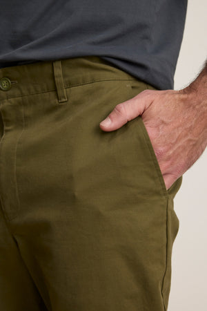 Wearing the MADDOX PANT by Velvet by Graham & Spencer in olive green and a dark gray shirt, the person has their right hand in their pocket, showcasing a polished look.