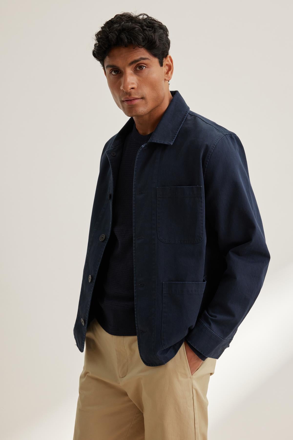   A person is wearing the Velvet by Graham & Spencer STEEL CHORE JACKET over a black shirt and beige pants against a neutral background. 