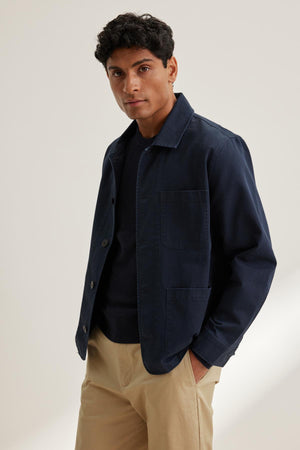 A person is wearing the Velvet by Graham & Spencer STEEL CHORE JACKET over a black shirt and beige pants against a neutral background.