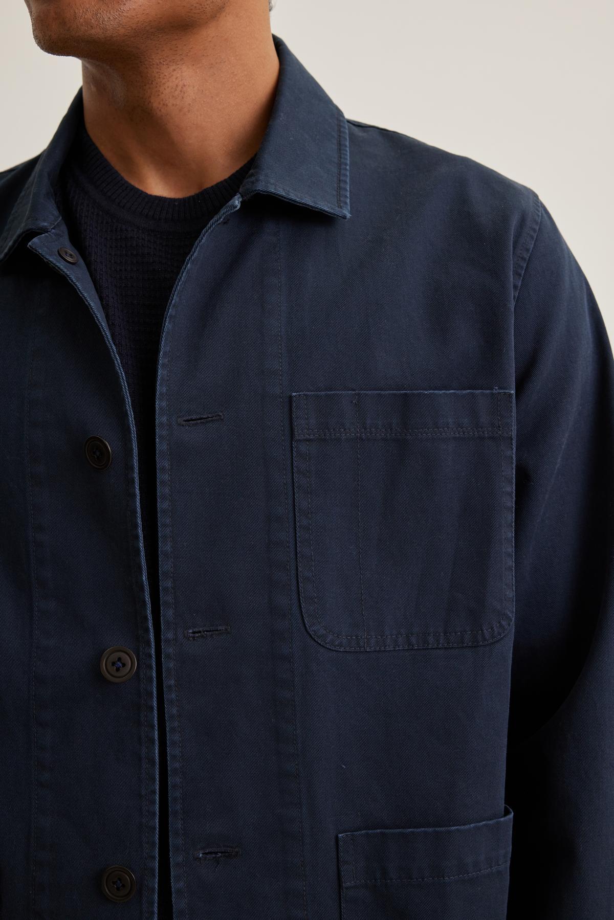   Someone wearing the STEEL CHORE JACKET in dark blue by Velvet by Graham & Spencer over a black textured shirt, facing slightly to the left. 