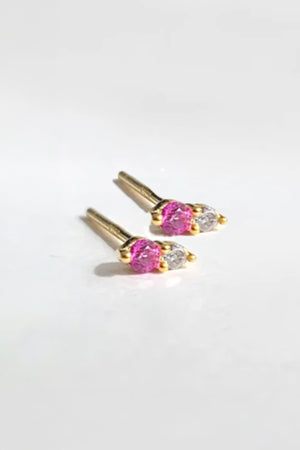 The TWIN STUD RUBY BY PHYLLIS AND ROSIE from Phyllis+Rosie is a beautifully hand-crafted pair of gold-studded earrings, each featuring one pink gemstone and one clear gemstone, displayed on a white background. Made with care in the heart of New York City.