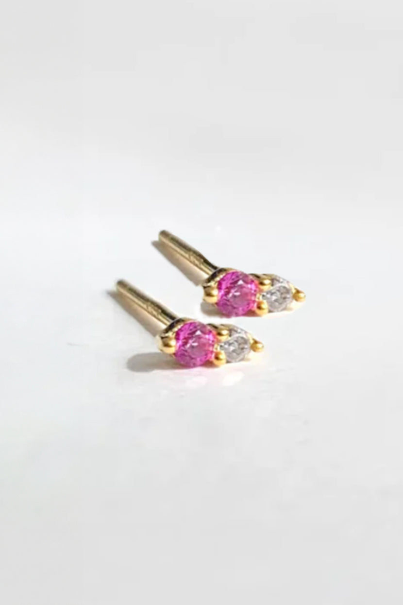 Close-up of TWIN STUD RUBY BY PHYLLIS AND ROSIE earrings showcasing pink and clear gemstones on a white background