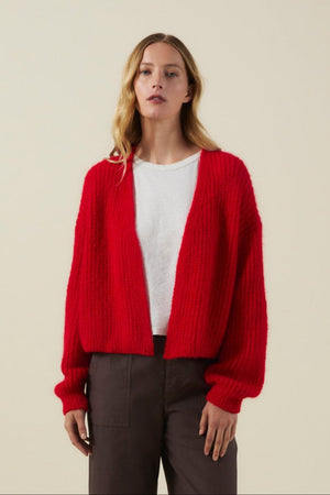 Wearing the Velvet by Graham & Spencer RANYA ALPACA CARDIGAN layered over a white T-shirt and dark pants, a woman stands against a plain beige background.