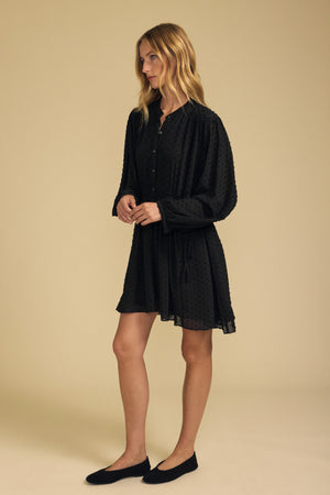 Velvet by Graham & Spencer BRINLEY TEXTURED CREPE DRESS, a black long-sleeved mini dress in textured crepe with a button-down bodice, styled for holiday parties with black ballet flats.