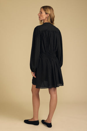 Back view of a person wearing a black Velvet by Graham & Spencer BRINLEY TEXTURED CREPE DRESS with a gathered waist, paired with black flats.