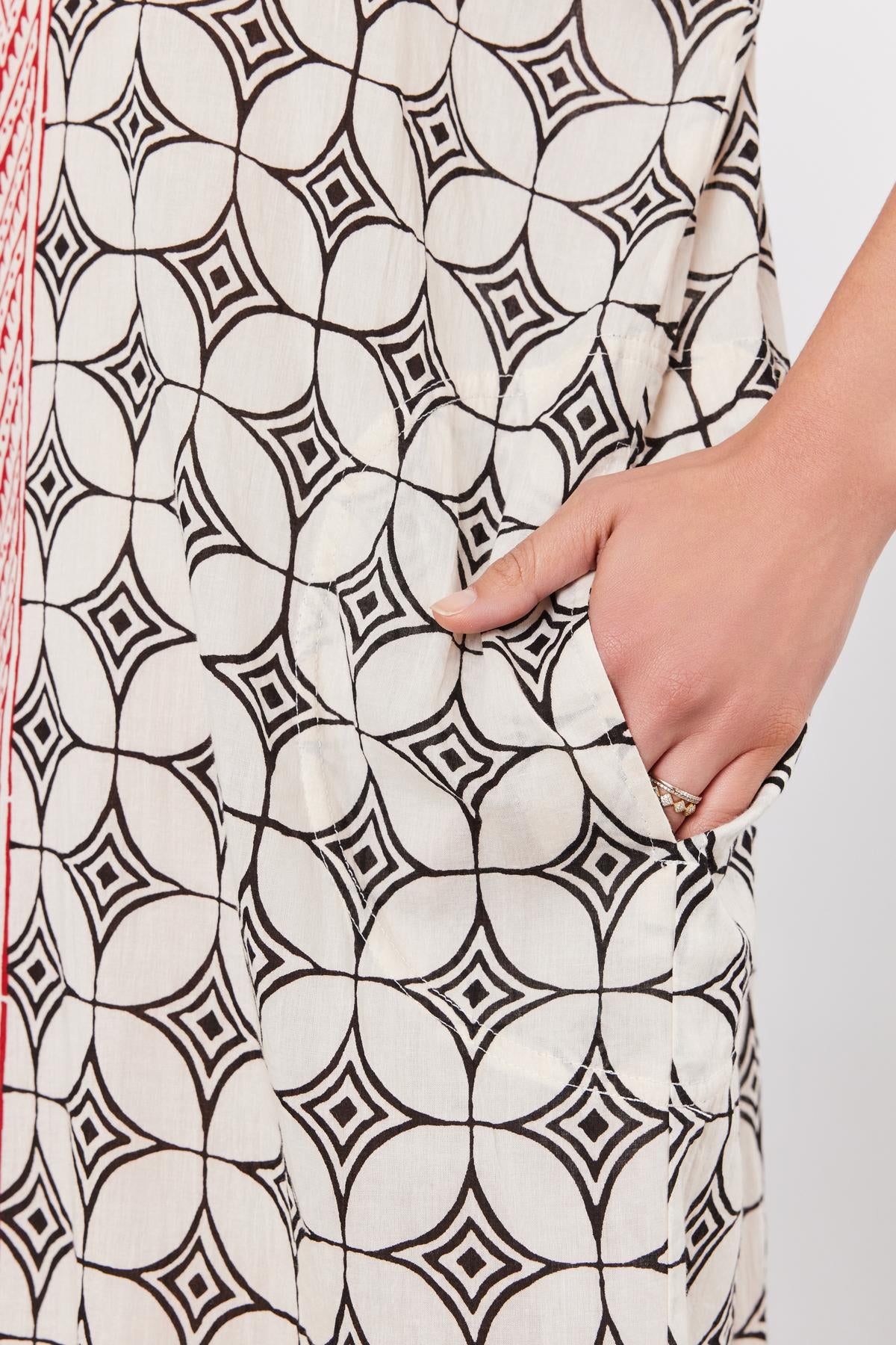   Close-up of a hand with a ring, touching a Velvet by Graham & Spencer Odessa Kaftan Dress with a black geometric pattern. 