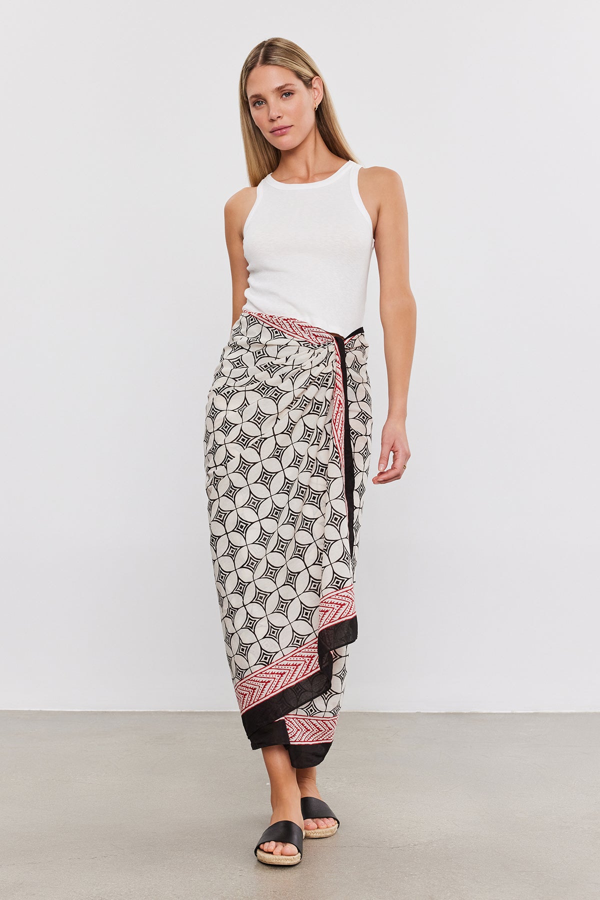 Woman wearing a white sleeveless top and a SARONG WRAP by Velvet by Graham & Spencer, standing on a beige floor against a plain white background.-37367009509569