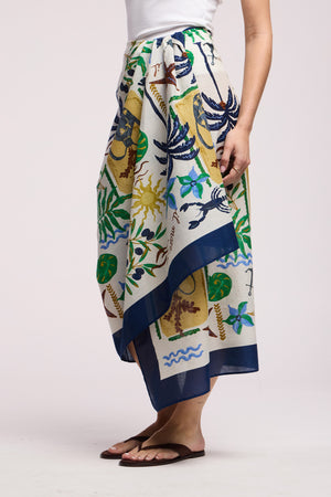 Model wears the ROBI SARONG by Velvet by Graham & Spencer as a wrap skirt, paired with a white sleeveless top and brown sandals; shown from mid-torso to feet.