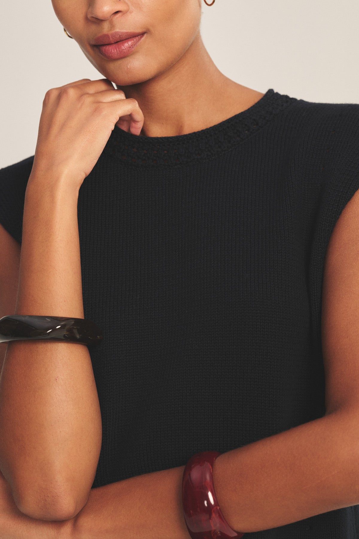 A woman wears the VANNY SWEATER, a sleeveless black pima cotton vest by Velvet by Graham & Spencer, styled with chunky black and dark red bangles—an effortlessly chic choice for transitional weather.