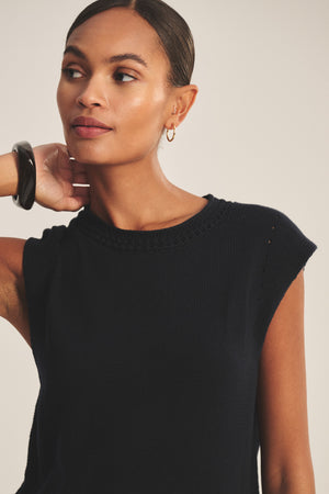 A woman with a neutral expression wears the VANNY SWEATER by Velvet by Graham & Spencer, styled with a black bracelet and small hoop earrings, her hair pulled back—an effortless look ideal for transitional weather.