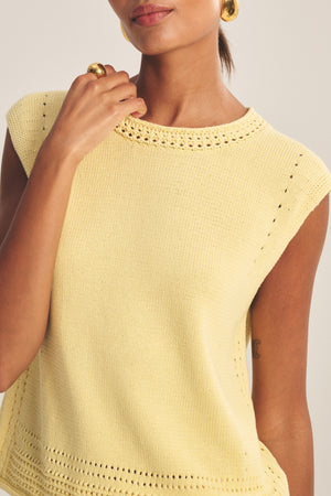 Wearing the VANNY SWEATER by Velvet by Graham & Spencer—a sleeveless yellow pima cotton vest with textured edges—plus gold hoop earrings and a gold ring, makes for an ideal transitional-weather look.