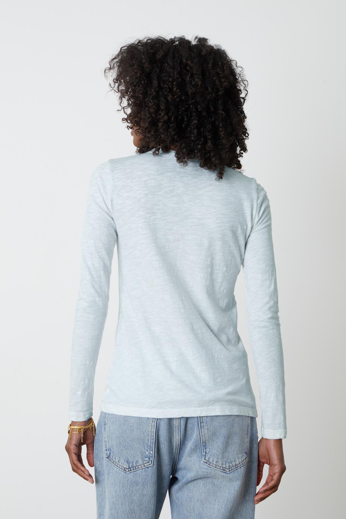 The back view of a woman wearing jeans and the Velvet by Graham & Spencer LIZZIE ORIGINAL SLUB LONG SLEEVE TEE.-35982858748097
