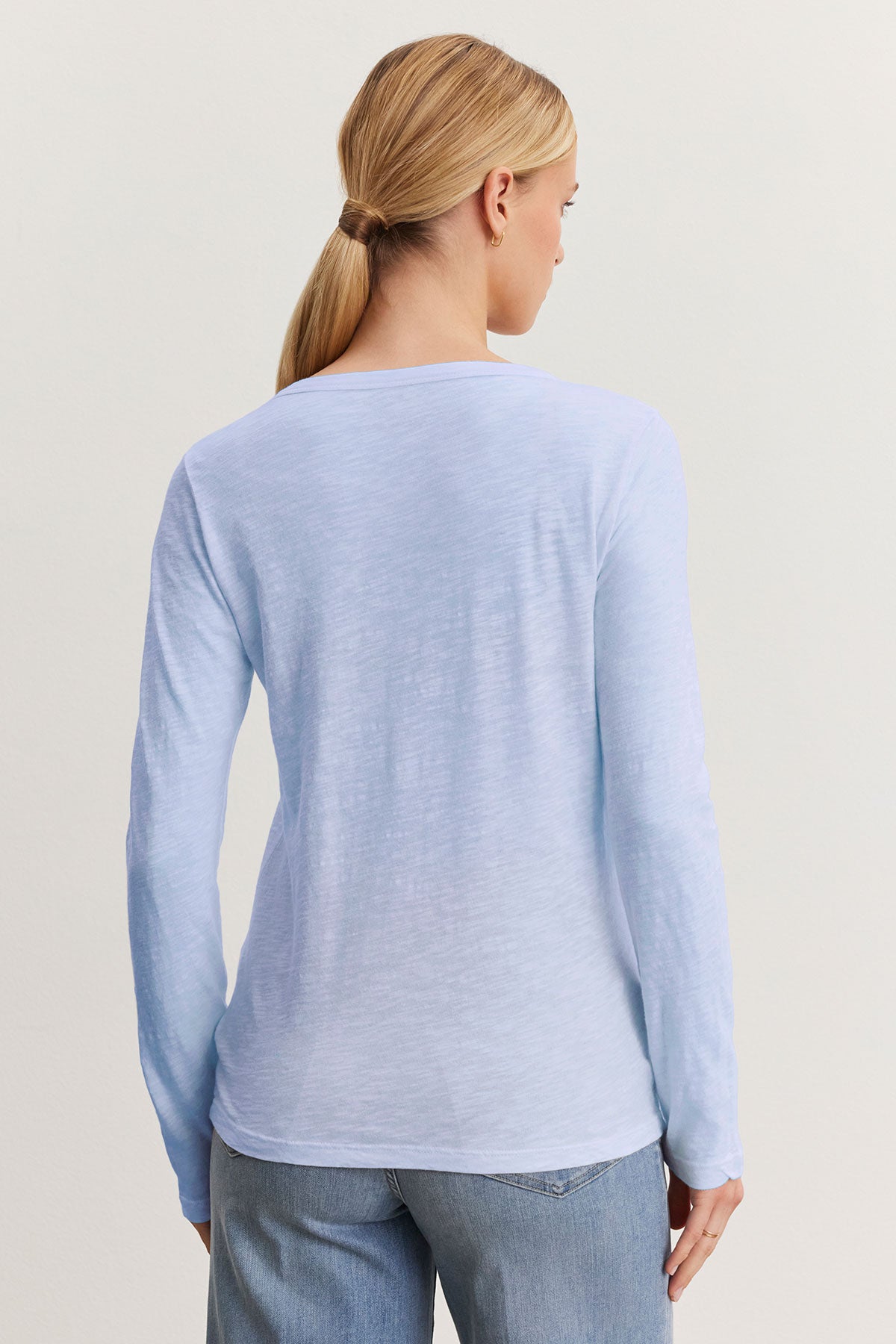   A person with long hair in a low ponytail, wearing Velvet by Graham & Spencer's LIZZIE TEE in light blue textured cotton slub and jeans, faces away. 