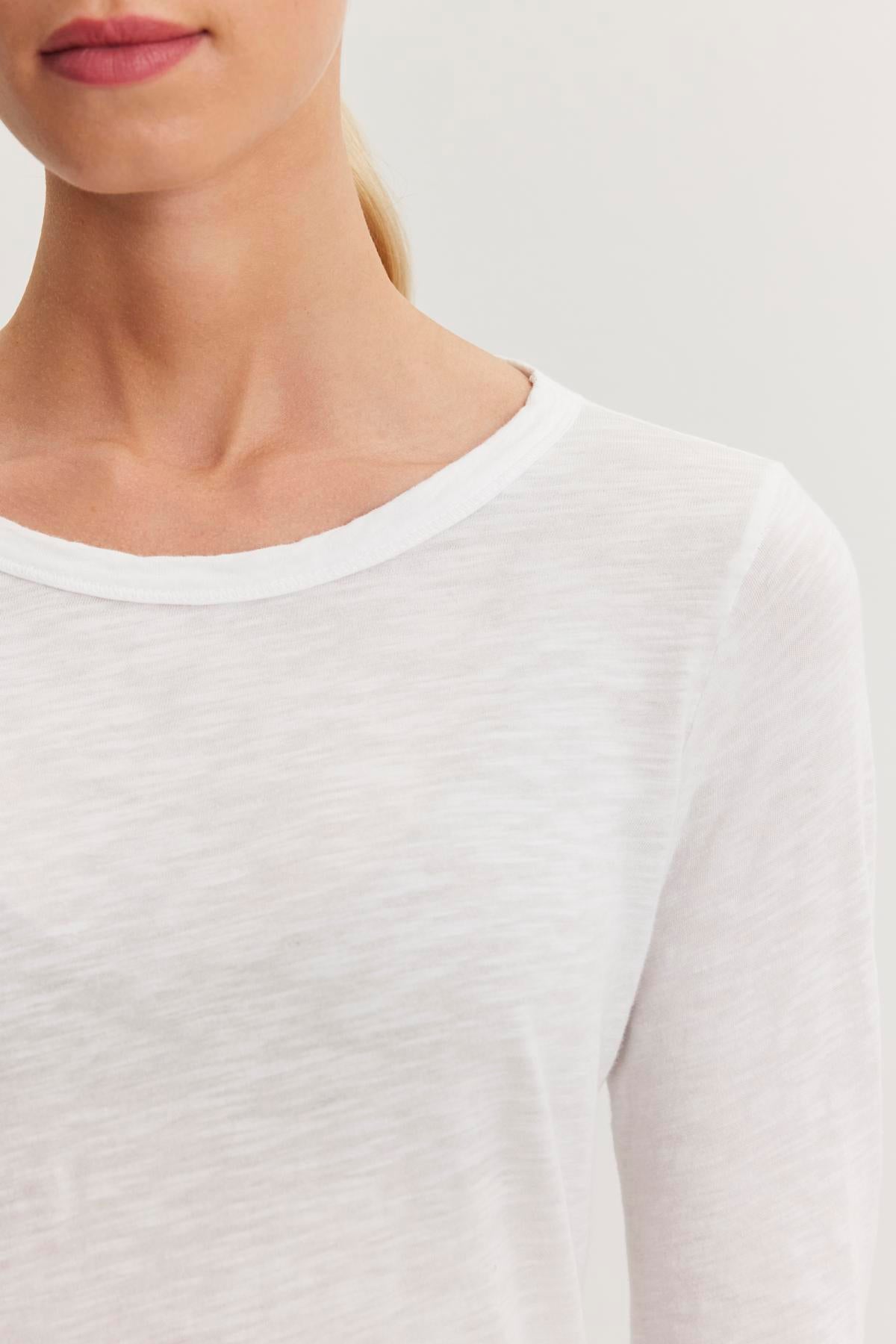   Close-up of the upper body of a person wearing a white, long-sleeve shirt made from textured cotton slub with a classic crew neckline, against a plain background. The shirt is the LIZZIE TEE by Velvet by Graham & Spencer. 