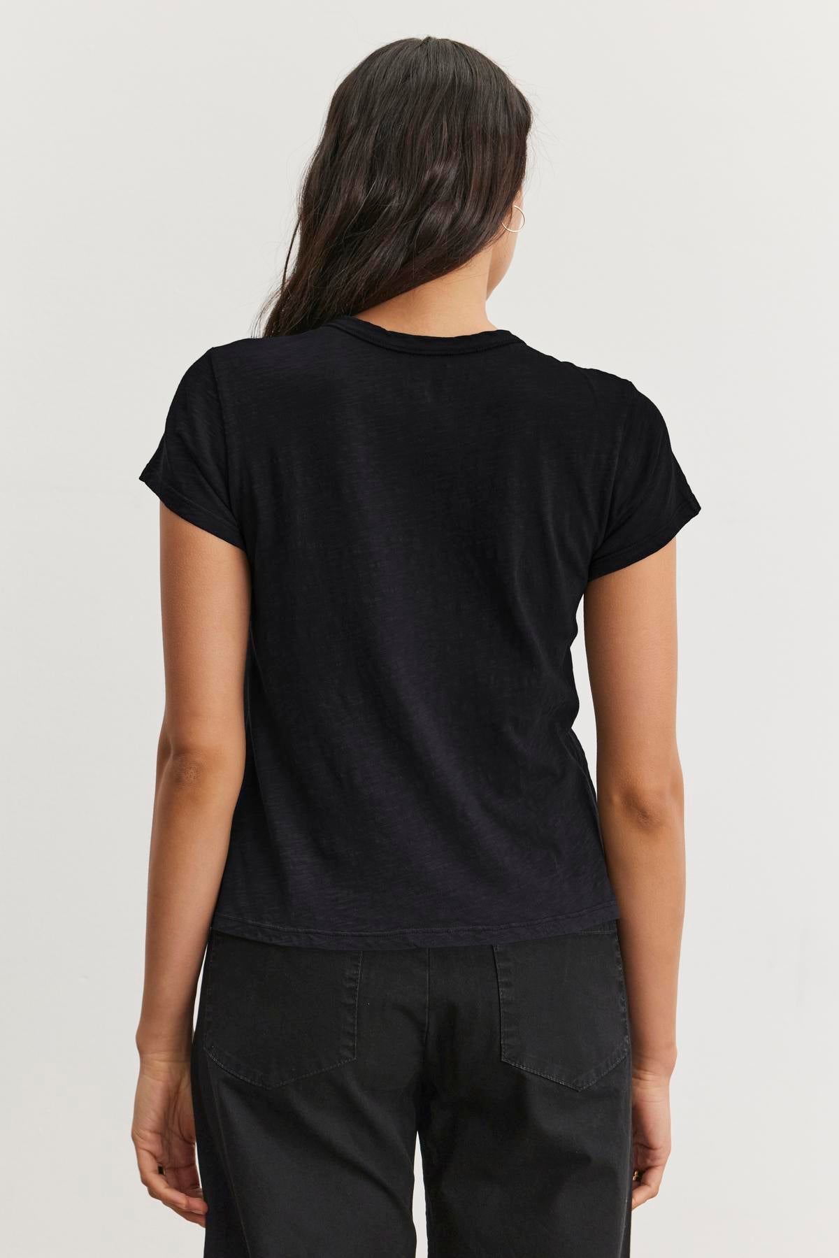   A person with long hair, dressed in a Velvet by Graham & Spencer MARIE TEE and dark pants, is shown from behind against a neutral background, perfect for a casual occasion. 