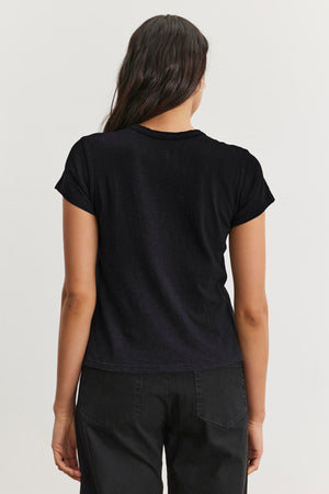 A person with long hair, dressed in a Velvet by Graham & Spencer MARIE TEE and dark pants, is shown from behind against a neutral background, perfect for a casual occasion.