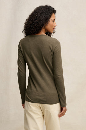 A person with curly hair is shown from the back, wearing the Velvet by Graham & Spencer LIZZIE TEE in olive green with beige pants, posing against a neutral background.