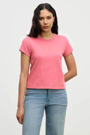 A person with long hair stands against a plain backdrop, wearing Velvet by Graham & Spencer's MARIE TEE in a relaxed boxy fit, paired with light blue jeans.