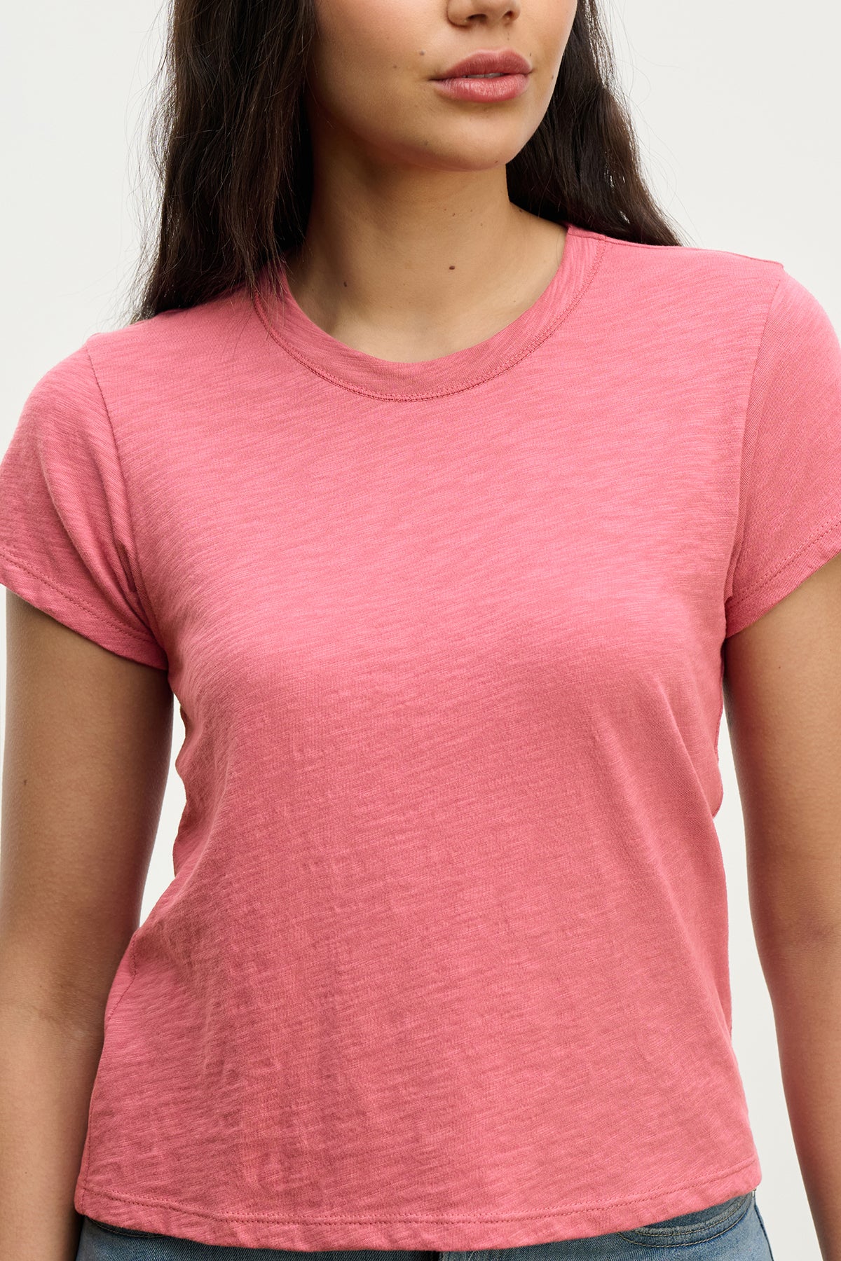   Against a neutral background, a woman stands wearing the MARIE TEE by Velvet by Graham & Spencer, a pink casual tee featuring a relaxed boxy fit. 